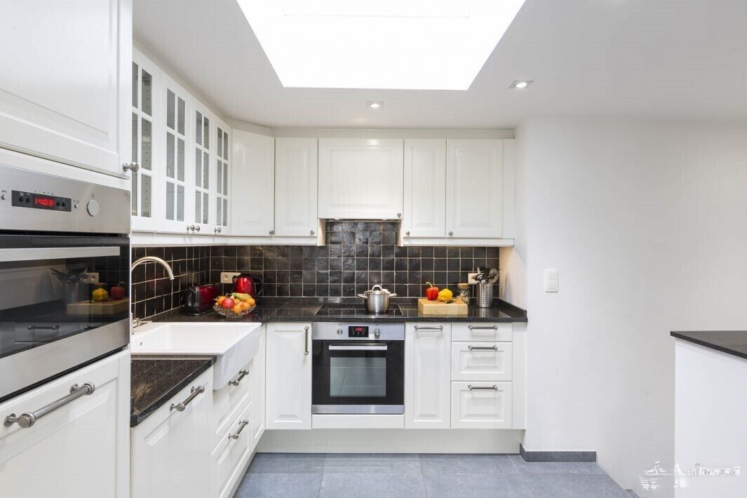 A modern kitchen with white cabinets, a black countertop, a built-in oven, and a skylight.