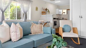 A modern living room with a blue sofa, a wooden chair, and a dining table. - Jetty Rd Jewel, Top Location, Wi-Fi, Parking, Chic (Brighton)