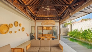 Area relax esterna coperta con piscina, mobili in legno e ventilatore a soffitto.