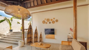 Un soggiorno moderno con un'ampia lampada a forma di ombrello intrecciato, una TV a schermo piatto montata a parete e una parete di pietra come sfondo.
