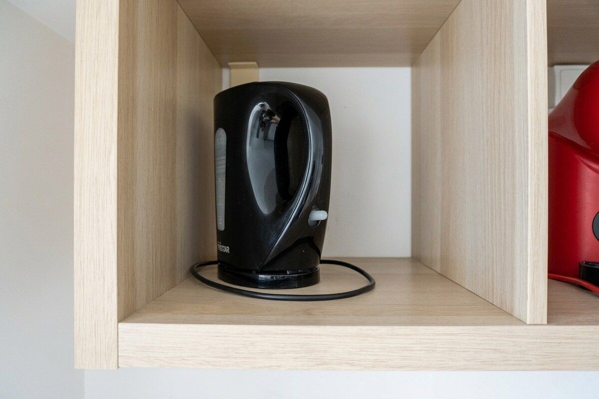 A black kettle on a wooden shelf in a kitchen cabinet.