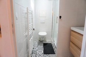 A bathroom with a white toilet, patterned floor tiles, a black mat, and a glass shower enclosure. - L’Épure - Terrasse & Parking Free (Tassin-la-Demi-Lune)