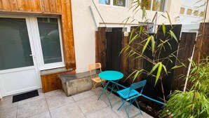 Um pátio com mesa e cadeiras, cerca de madeira e planta de bambu.