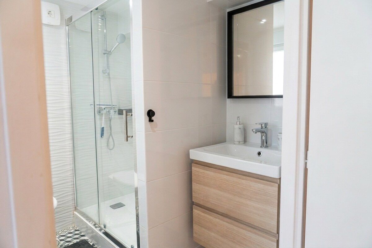 Een moderne badkamer met een douche in glazen cabine, een witte wastafel en houten kastjes.