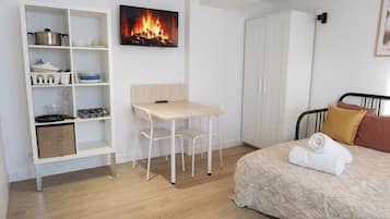 Een slaapkamer met een bed, nachtkastje, stoel, kledingkast en een wandplank met keukengerei.