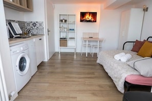 A compact room with a washing machine, a small table, a bed, and a wall-mounted fireplace. - L’Épure - Terrasse & Parking Free (Tassin-la-Demi-Lune)