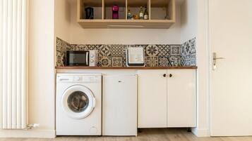 A laundry area with a washing machine and dryer, a microwave, and a shelf with bottles.
