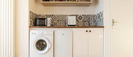 A laundry area with a washing machine and dryer, a microwave, and a shelf with bottles.