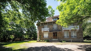 A two-story stone building with a balcony, a front porch, and a gravel driveway. - DEMEURE DU SAULE MADAME (Thieux)