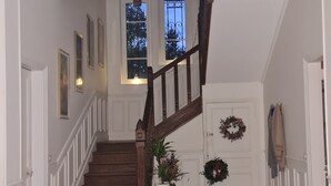 A staircase with a wooden handrail leading to a landing with a checkered floor and a door with a wreath. - DEMEURE DU SAULE MADAME (Thieux)