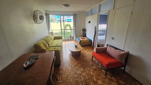 Een woonkamer met een bank, een rode slaapbank, een salontafel en een houten vloer.