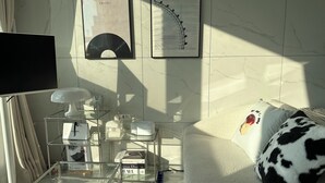 A modern living room with a glass coffee table, a white sofa with a cow print pillow, and a wall-mounted TV.