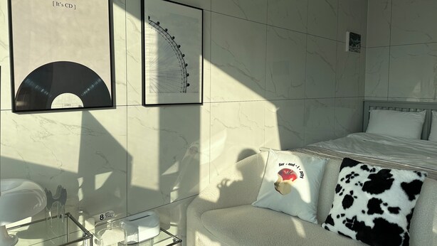 A hotel room with a bed, a sofa, a glass coffee table, and framed pictures on the wall.