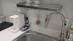 A kitchen with a stainless steel sink, a coffee maker, a tea kettle, and a bottle of hand soap.