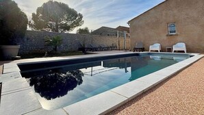 Une piscine rectangulaire aux bords nets, entourée d’un mur de pierre et d’un bâtiment doté d’une fenêtre.