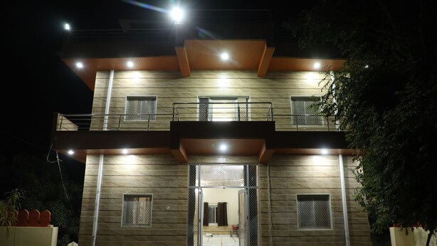 A modern two-story building with a balcony on the upper floor, a large entrance with glass doors, and a small window on the ground floor. - Eagle Farm Stay Pushkar (Pushkar)