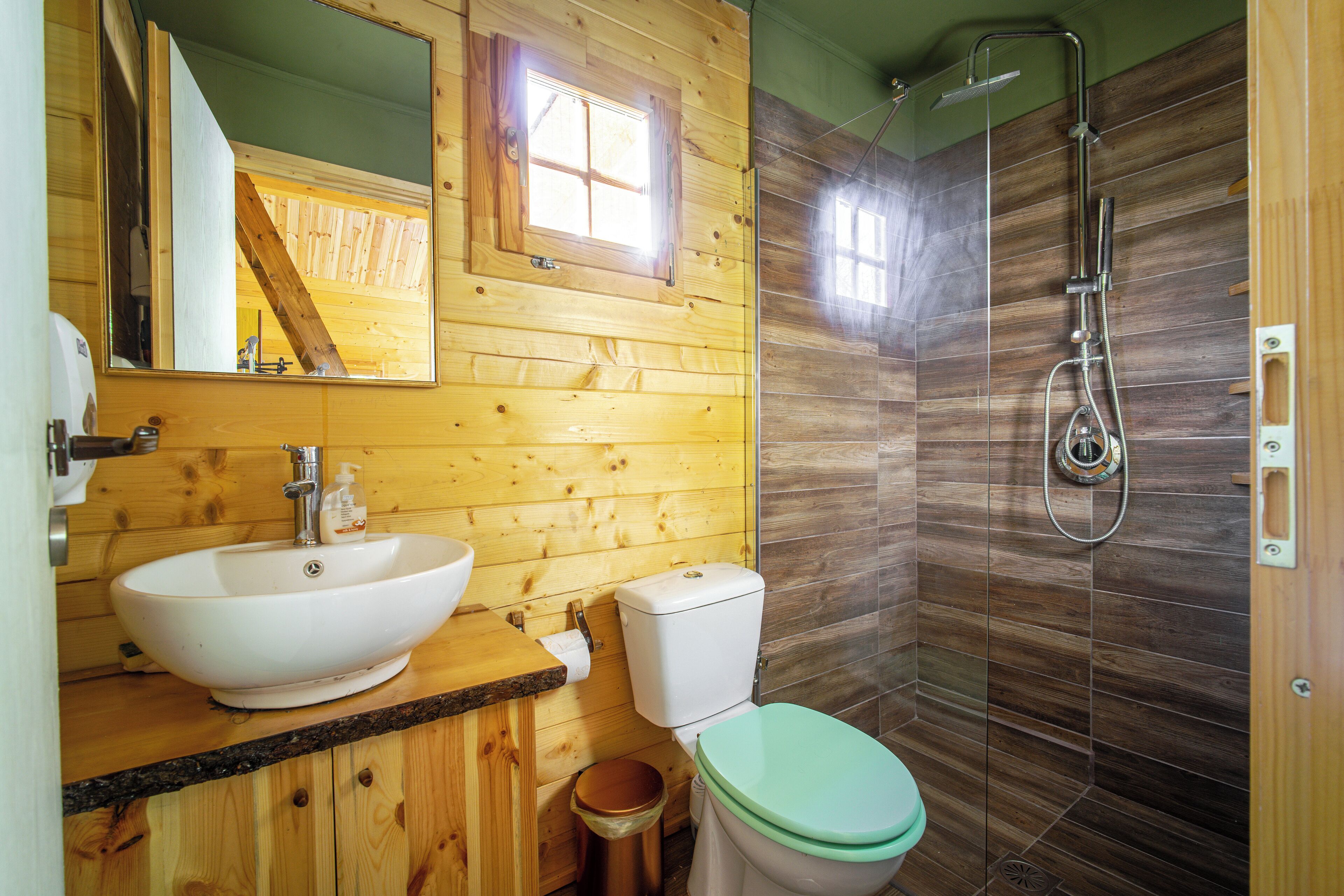 A wooden cabin bathroom with a large sink, toilet, and shower.