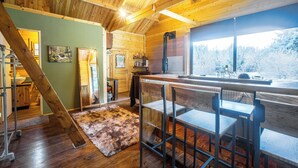 Interior de madera con una zona de bar, vigas de madera en el techo y vistas a un bosque nevado a través de un ventanal grande.
