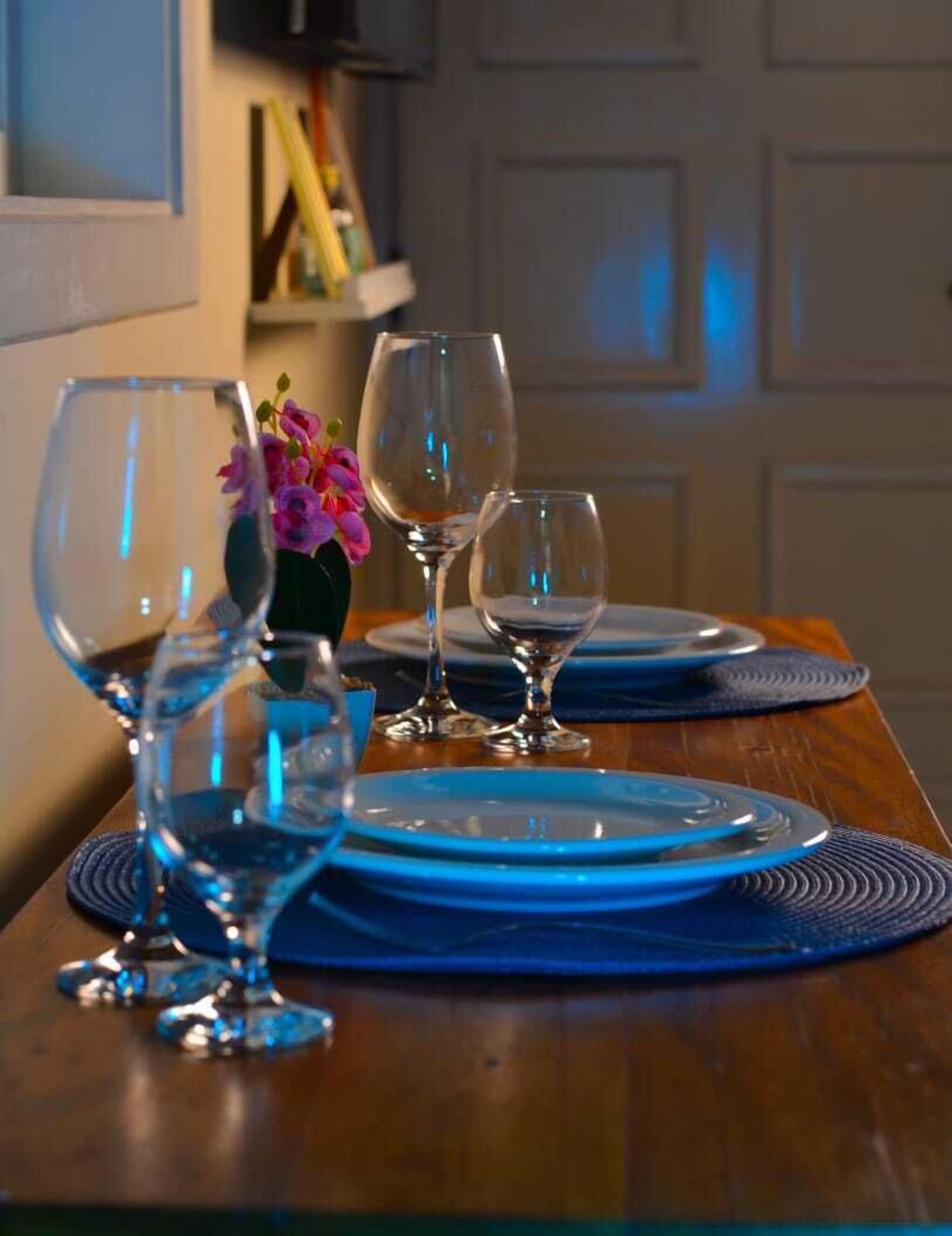 A dining table with blue plates and wine glasses, a vase with pink flowers, and a wooden table.