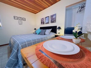 A bedroom with a bed, bedside tables, a dining table with a plate and cutlery, and wall art. - Da Matta House (Campos do Jordão)