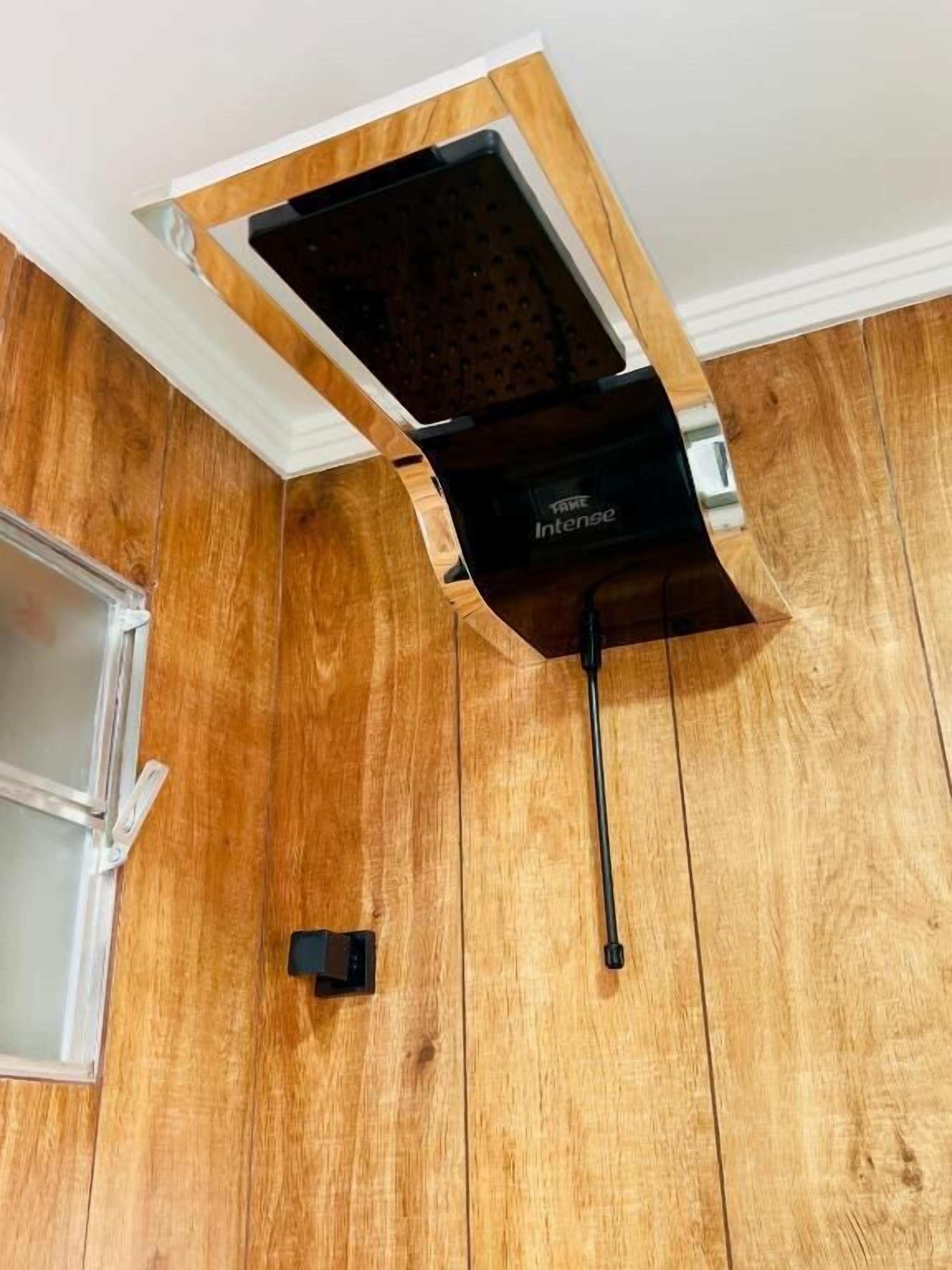 Esquina de una habitación con suelo de madera, pared blanca y un electrodoméstico negro con la etiqueta 'TAKE Intense'.