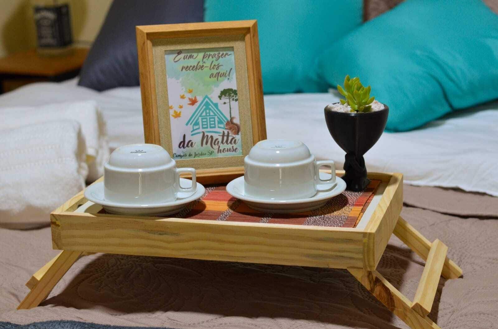 Ein Holztablett mit zwei weißen Tassen und Untertassen, einem gerahmten Schild mit Text und einem kleinen Blumentopf auf einem Bett mit Kissen.