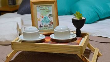 Ein Holztablett mit zwei weißen Tassen und Untertassen, einem gerahmten Schild mit Text und einem kleinen Blumentopf auf einem Bett mit Kissen.