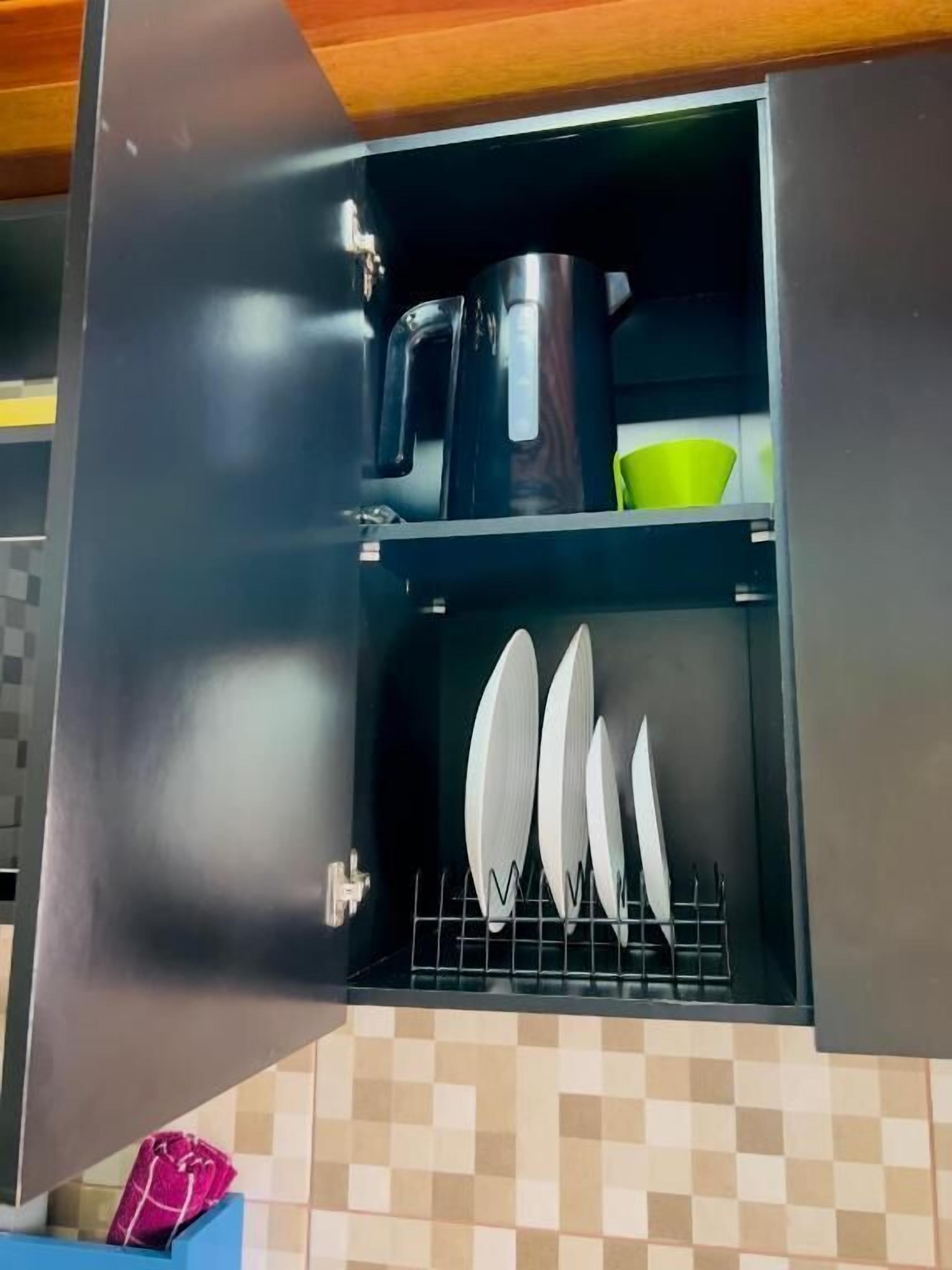 A kitchen with a microwave, a green bowl, and a rack with white plates.