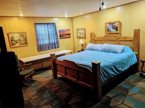 A wooden-paneled room with a bed, a bench, and a desk.
