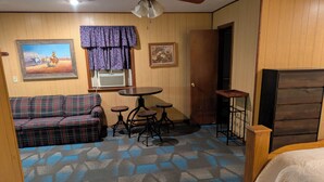 Ein Zimmer mit einem karierten Sofa, einem runden Tisch mit Hocker, einer Holztür und einem Bett mit weißer Bettdecke.