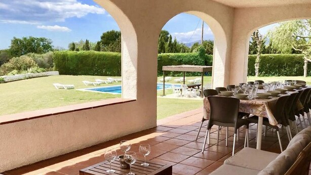 Zona d'estar a l'aire lliure coberta amb vista a una piscina i un jardí.
