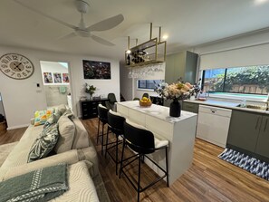 A modern kitchen with a central island, bar stools, a ceiling fan, and a dining area with a sofa and chairs. - East Gippsland Retreat for you and your Furry Friends. A home away from home. (East Bairnsdale)
