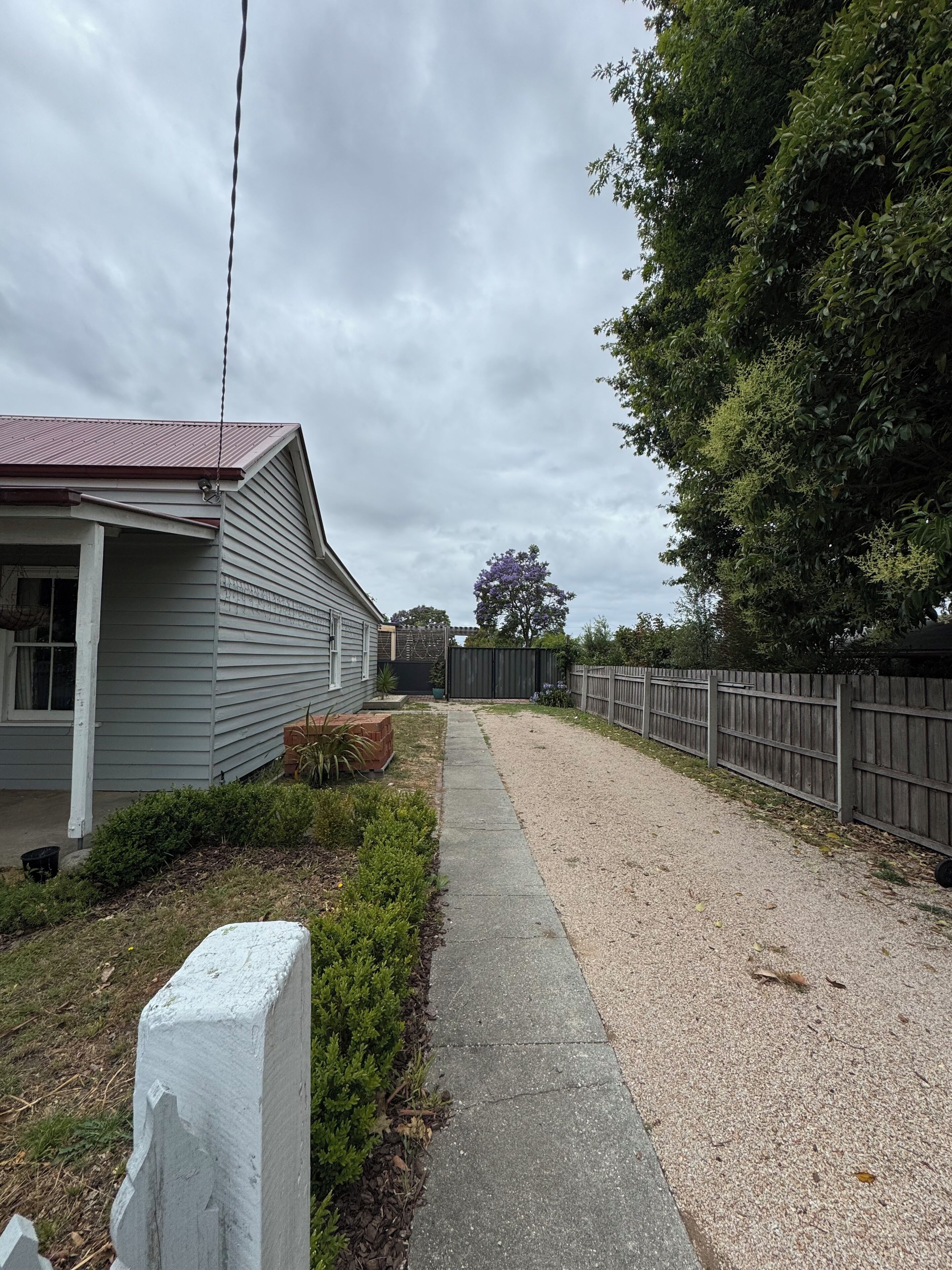 A residential property with a gravel driveway, a wooden fence, and a house with a red roof.