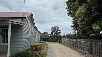 A residential property with a gravel driveway, a wooden fence, and a house with a red roof.