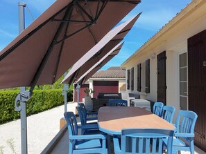 Eine Terrasse mit Tisch, Stühlen, einem Grill und einem überdachten Bereich mit Sonnenschirmen.
