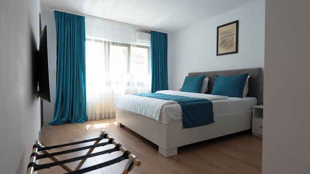 A bedroom with a bed, curtains, a television, and a framed picture on the wall. - 3 Baneasa Airport (Bucharest)
