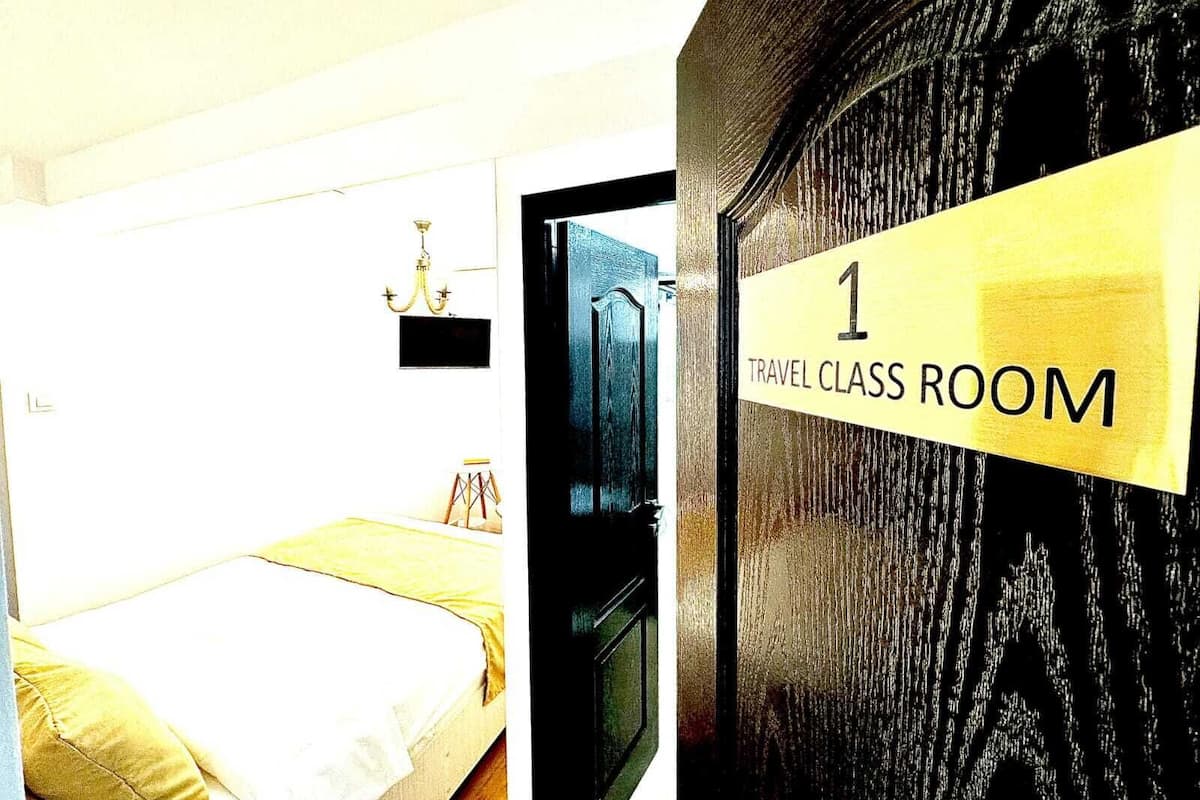 A travel class room with a bed, a small table, and a chandelier.
