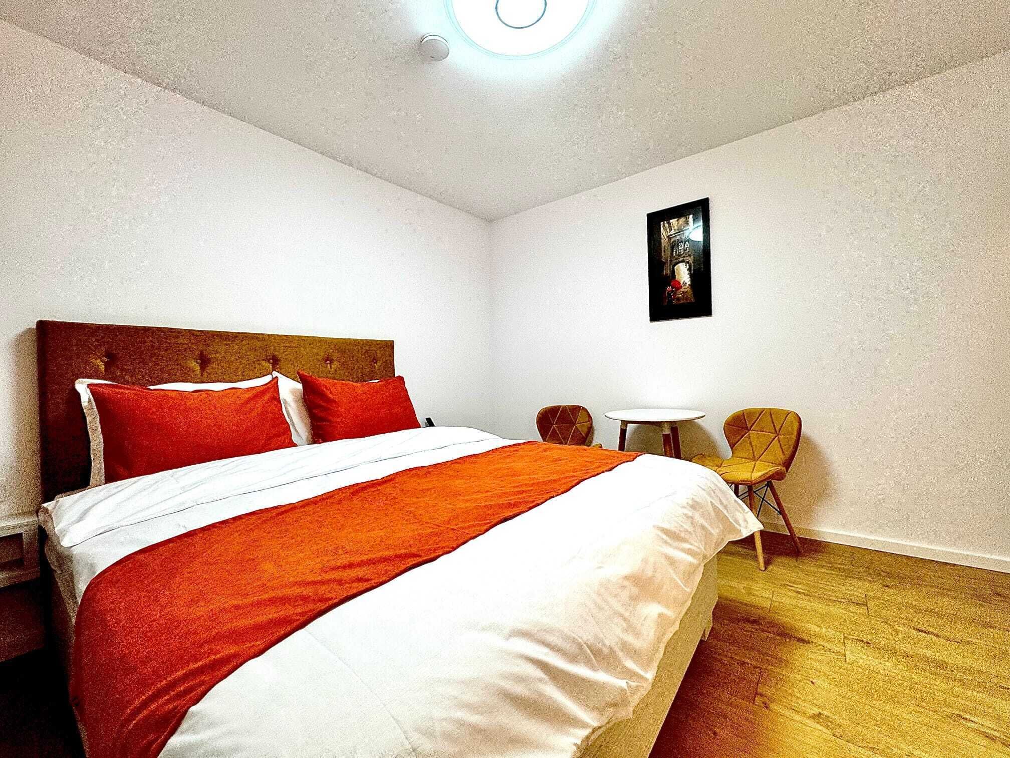 A hotel room with a large bed, a small round table, two chairs, and a painting on the wall.