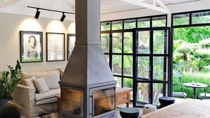 A modern living room with a large fireplace, comfortable seating, and large windows offering a view of greenery. - Long stay suite for rent in Bitez w balcony, pool, wi-fi (Bodrum)