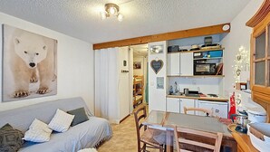 Ett mysigt vardagsrum med en soffa, ett matbord och stolar. Det finns ett köksområde med skåp och en mikrovågsugn. En tavla med ett motiv av en isbjörn hänger på väggen.