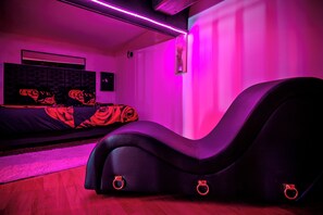 A modern bedroom with a curved black sofa, a bed with rose-patterned bedding, and a wall-mounted TV. - Love Room Perpignan • Jacuzzi, Tantra, Swing & Air Conditioning (Perpignan)