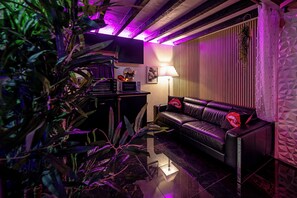 A modern living room with a leather sofa, a flat-screen TV, and a dining area with a microwave. - Love Room Perpignan • Jacuzzi, Tantra, Swing & Air Conditioning (Perpignan)