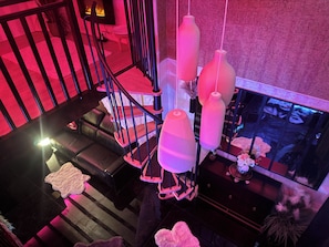 Un escalier avec une rampe noire, un canapé en cuir et un luminaire décoratif suspendu.