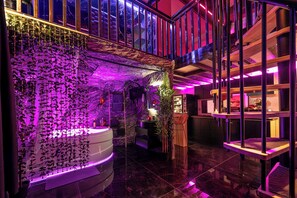 A modern interior with a curved reception desk, a staircase, and a glass railing. - Love Room Perpignan • Jacuzzi, Tantra, Swing & Air Conditioning (Perpignan)
