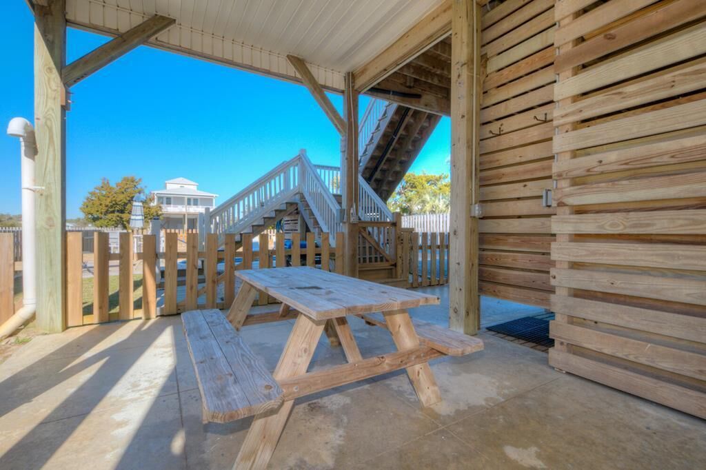 A wooden deck with picnic tables, a covered area, and a staircase leading to a building.