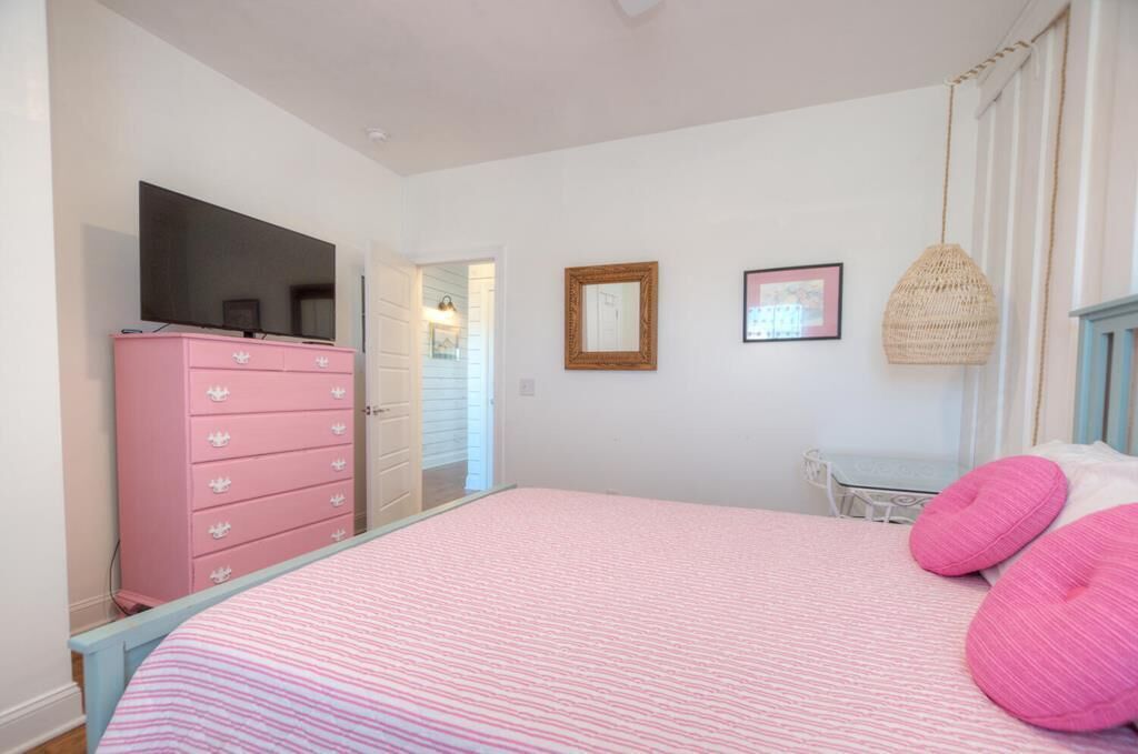 A bedroom with a pink bedspread, a pink dresser, and a television on the left wall.