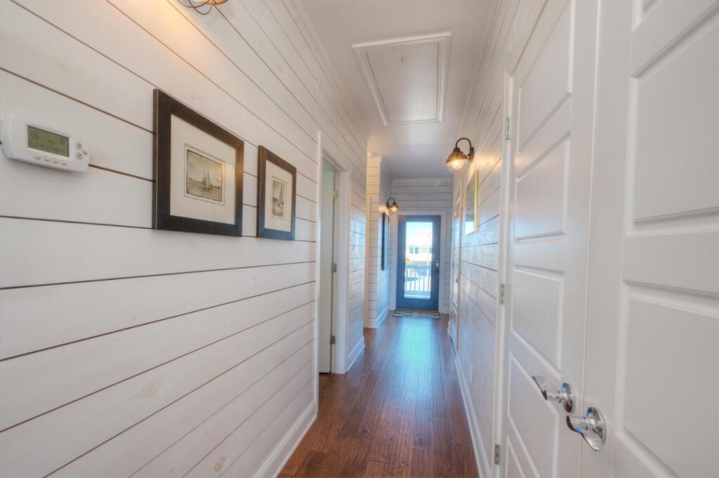 A hallway with white wooden walls, framed pictures, and a thermostat.