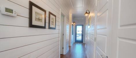 A hallway with white wooden walls, framed pictures, and a thermostat.
