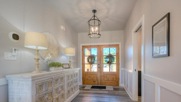 A hallway with a wooden door, a white console table with lamps, and a ceiling light fixture. - The Bat Cave at OKI: Cozy 3BR retreat in Oak Island, near beaches and mini golf! (Oak Island)