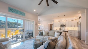 A spacious living room with a large sectional sofa, a coffee table, and yellow chairs outside the sliding glass door. - The Bat Cave at OKI: Cozy 3BR retreat in Oak Island, near beaches and mini golf! (Oak Island)